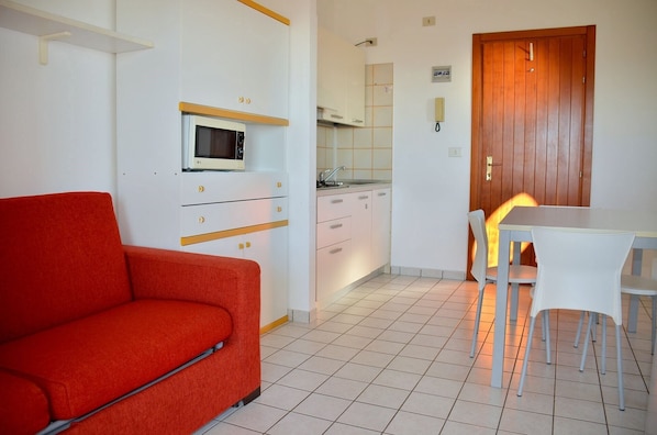 A compact living space with a kitchenette, a dining area with a table and chairs, and a red sofa.