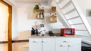 Uma cozinha compacta com armários brancos, pia, micro-ondas e prateleiras de madeira com plantas e utensílios de cozinha.