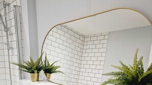 Un bany modern amb rajoles blanques, un lavabo blanc i dues plantes de fusta en testos.
