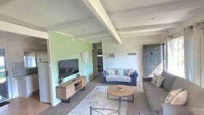 Un amplio salón con televisor de pantalla plana, sofá, mesa de centro y zona de cocina con refrigerador y microondas.
