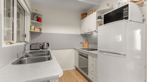Cocina compacta con lavamanos, tostadora, hervidor, horno y refrigerador blanco.