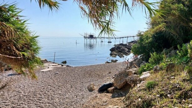 A beach with pebbles, a rocky area, and a pier extending into calm water.