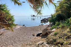 Une plage de galets, une zone rocheuse et une jetée qui s’avance dans une eau calme.