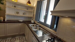 A kitchen with a gas stove, two sinks, a window with blinds, and decorative plates on shelves.