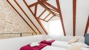 Una habitació amb dos llits, un amb llençol vermell i l'altre amb almoina beix. La habitació té una paret de pedra i bigues de fusta al sostre.