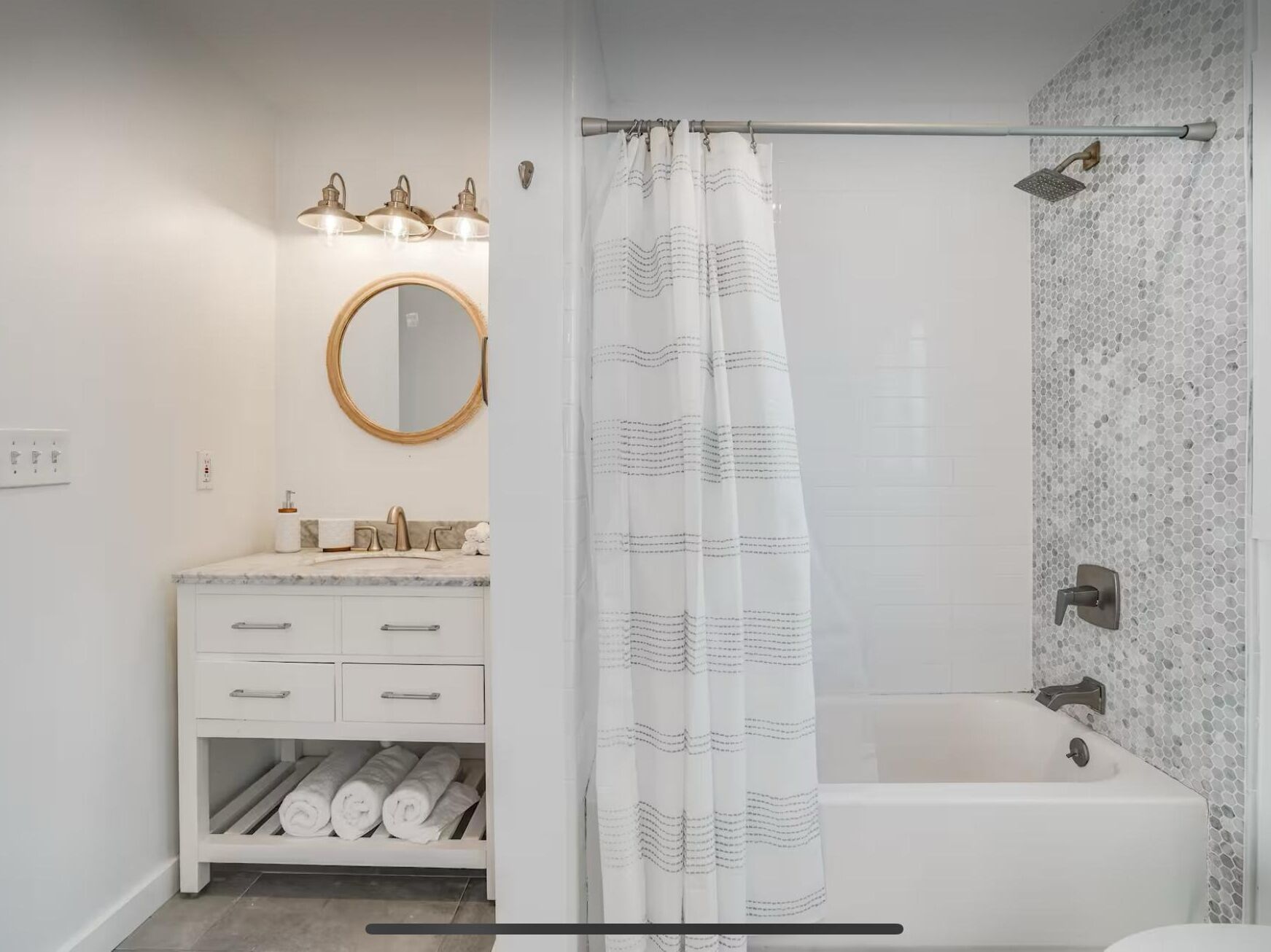 A modern bathroom with a white vanity, a round mirror, a shower with a patterned curtain, and a tiled wall.
