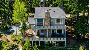 A two-story house with a stone chimney, a balcony, and a patio with outdoor furniture.