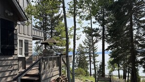 A wooden cabin with a deck, surrounded by trees and a lake view.