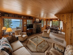 Interior acogedor de una cabaña con chimenea, asientos cómodos y un ventanal grande con vistas a un lago.