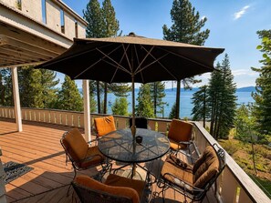 Eine Terrasse mit einem runden Tisch und Stühlen, einem Sonnenschirm und Blick auf das Meer und Bäume.