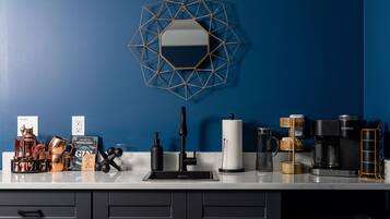 A kitchen with a blue wall, a geometric mirror, a coffee maker, a kettle, and various kitchenware.