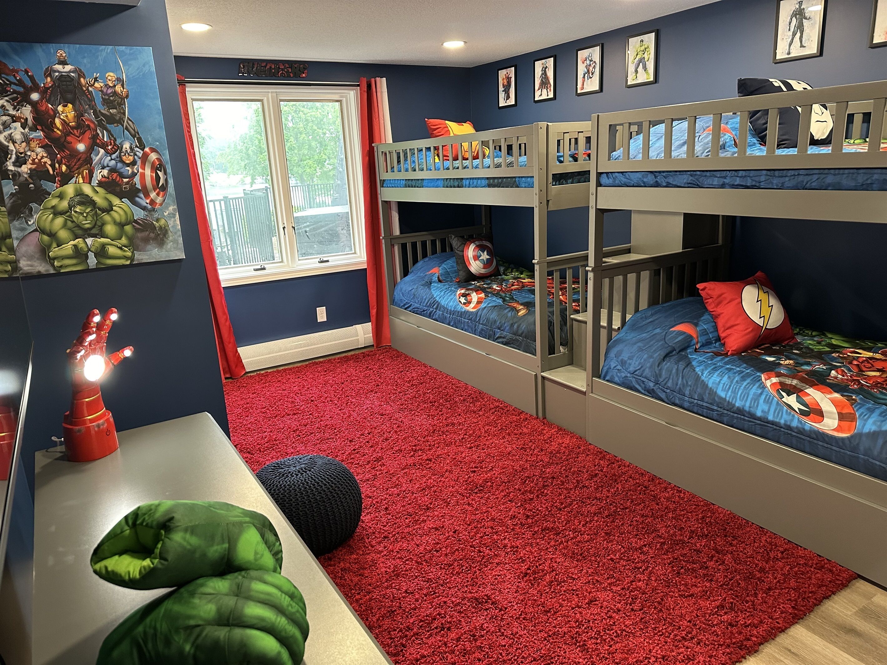 A room with bunk beds, a red carpet, and superhero-themed bedding.