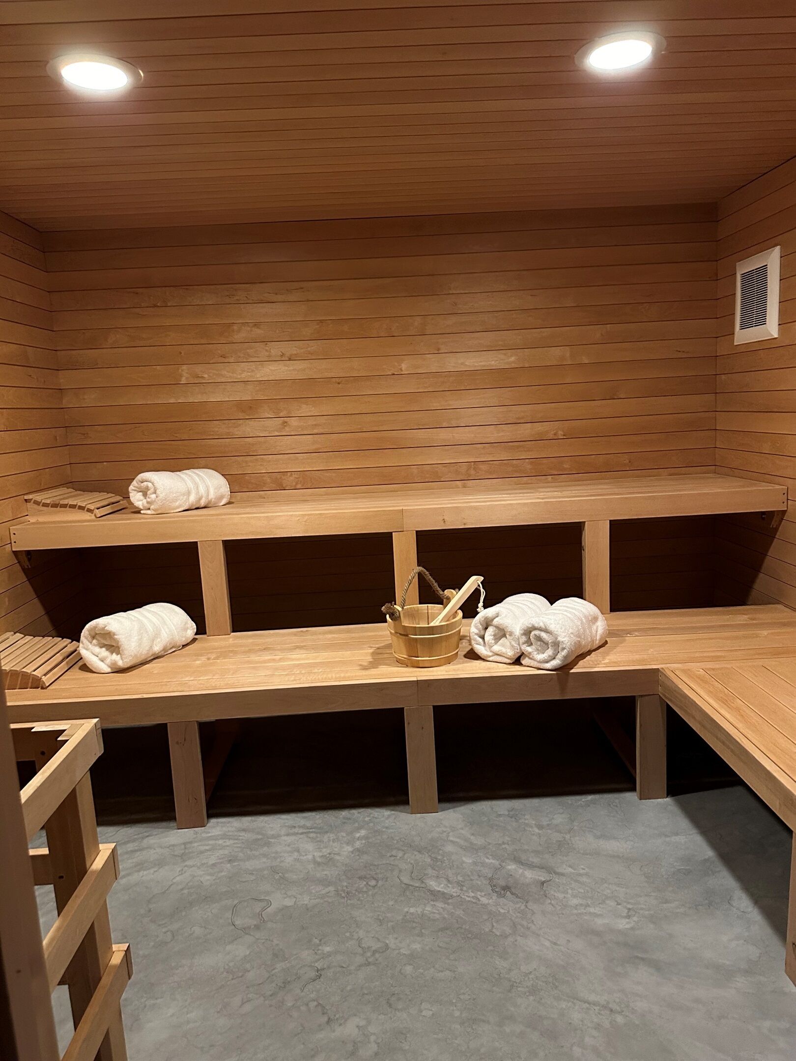 Una sala de sauna con bancos de madera y suelo de madera, y un techo con iluminación empotrada.