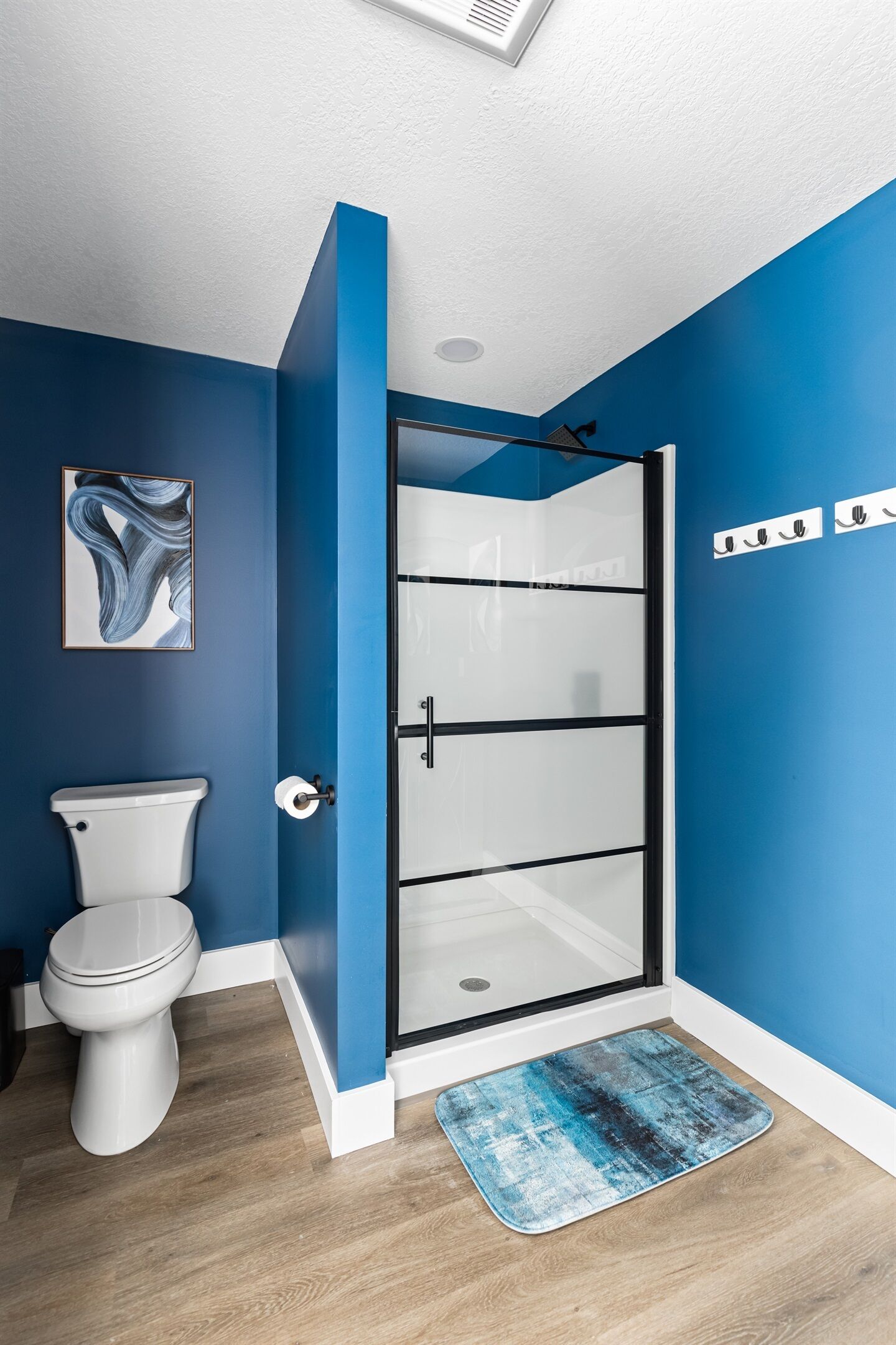 A bathroom with a white toilet, a glass shower enclosure, and a blue wall.