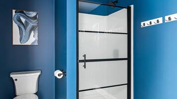 A bathroom with a white toilet, a glass shower enclosure, and a blue wall.