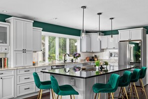 Una cucina moderna con mobili bianchi, un'isola centrale con sgabelli da bar e illuminazione a sospensione.