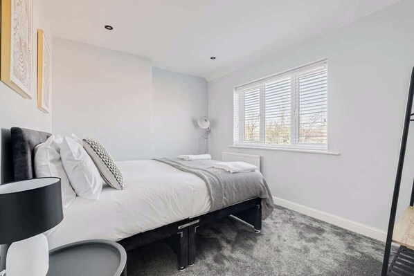 A bedroom with a bed, bedside lamp, and a window with blinds.