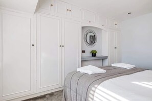 A bedroom with a large bed, a wardrobe, and a mirror with a circular design. - Stylish 3 Bedroom House With Parking (Bedford)