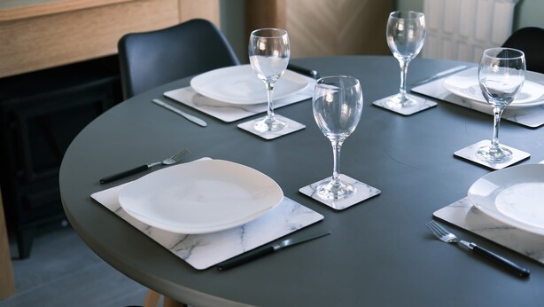 Une table de salle à manger ronde, avec de l’assiette blanche, des couverts en argent et des verres à vin transparents, le tout disposé pour quatre personnes.