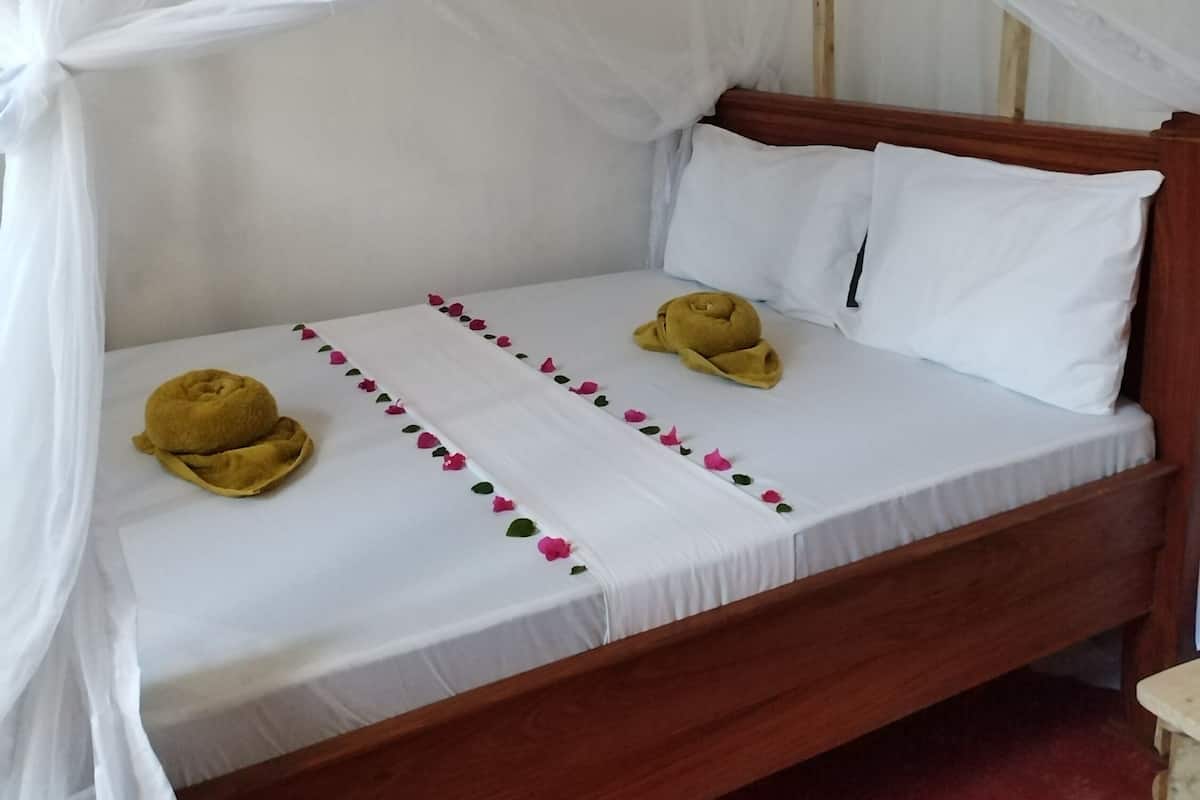 A single bed with a wooden frame, white bedding, and a mosquito net.