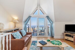 A cozy living room with a brown leather sofa, a coffee table with a board game, a TV, and a balcony with a view. - Schooner House - Panoramic Sea Views and Parking (Saundersfoot)