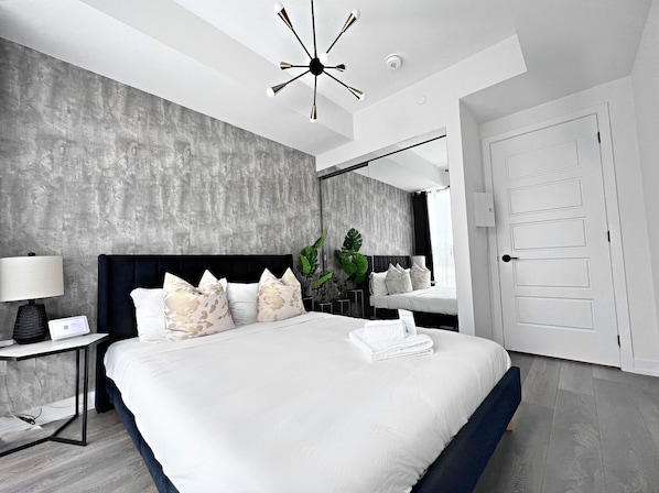 Une chambre à coucher moderne avec un grand lit, une table de chevet avec une lampe, un miroir et une porte.
