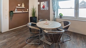 Een eethoek met een ronde tafel, vier stoelen, een potplant en decoratieve spullen op planken.