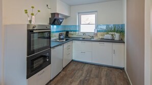 Een moderne keuken met witte kastjes, een zwarte oven en een raam met uitzicht op zee.