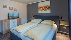 Een moderne slaapkamer met een bed, nachtkastjes, een televisie en kunst aan de muur.