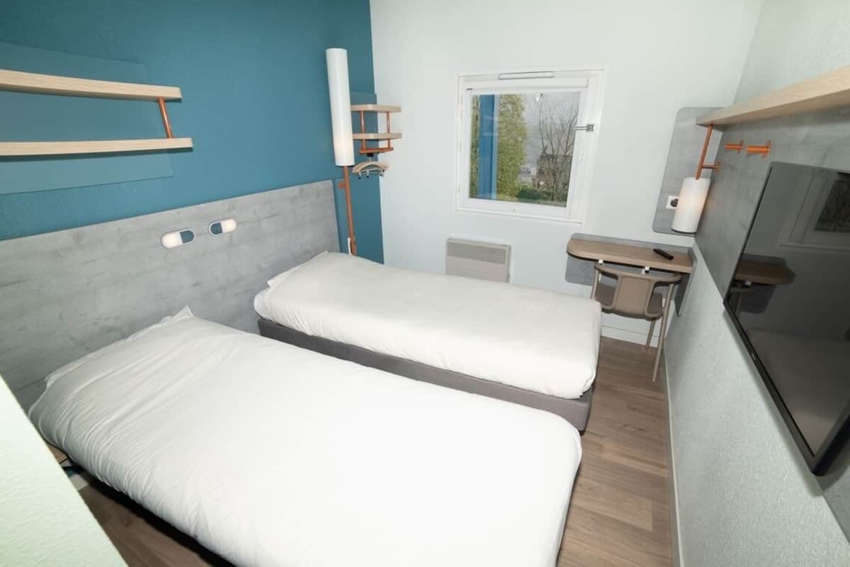 A compact room with two beds, a small desk, a window, and a TV.