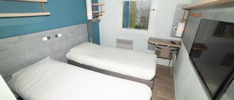 Una habitación pequeña con dos camas, un escritorio, una ventana y un televisor.