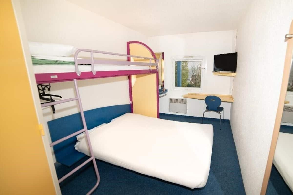 A bunk bed room with a desk and chair, a television, and a window.