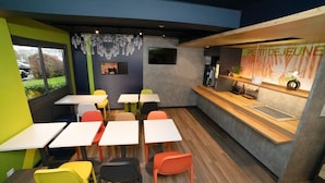 A modern cafe with colorful chairs and tables, a counter with a menu, and a view of the outdoors. - Accueil Hotel Besançon (Besancon)