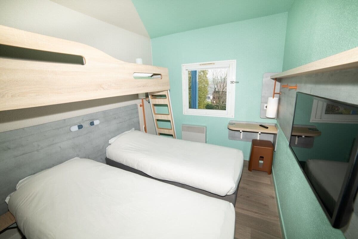 A compact room with bunk beds, a small window, a desk, and a chair.