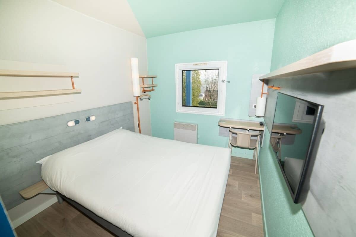 A bedroom with a bed, a window, a bedside table, and a mirror.