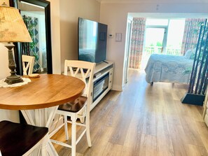 Een kamer met een houten eettafel, witte stoelen, een televisie en een bed met uitzicht.