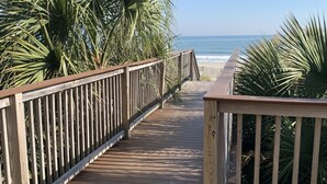 A wooden boardwalk leading to a beach with palm trees on either side. - Oceanfront Condo, Balcony, Pools, Beach Access, Walk to Restaurants & Boardwalk  (Myrtle Beach)
