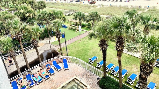 A beach resort with a pool area, palm trees, and a pier in the background. - Oceanfront Condo, Balcony, Pools, Beach Access, Walk to Restaurants & Boardwalk  (Myrtle Beach)