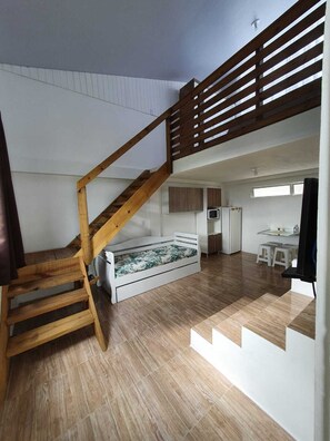 A loft-style room with a wooden staircase, a bunk bed, a kitchenette, and a dining area. - Pousada Korb (Santo Amaro da Imperatriz)