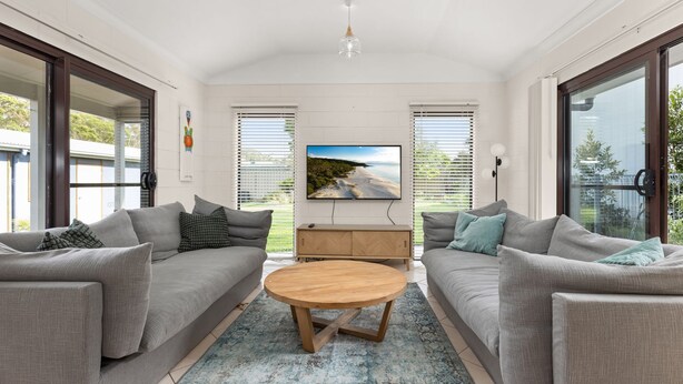 A modern living room with a grey sofa set, a wooden coffee table, and a flat-screen TV mounted on the wall.
