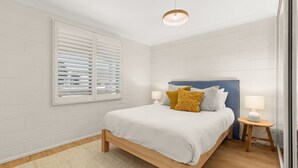 A bedroom with a bed, two bedside tables, a window with blinds, and a ceiling light.