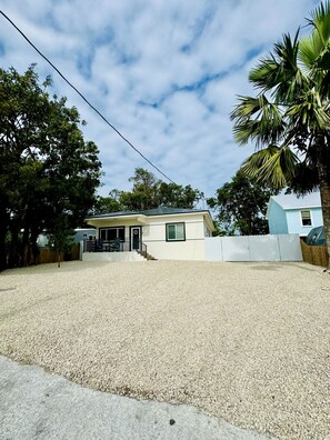 A single-story house with a gravel driveway, a front porch, and a fenced yard. - Snowbird specials!! Book now. Minimum stay 28 days. (Key Largo)