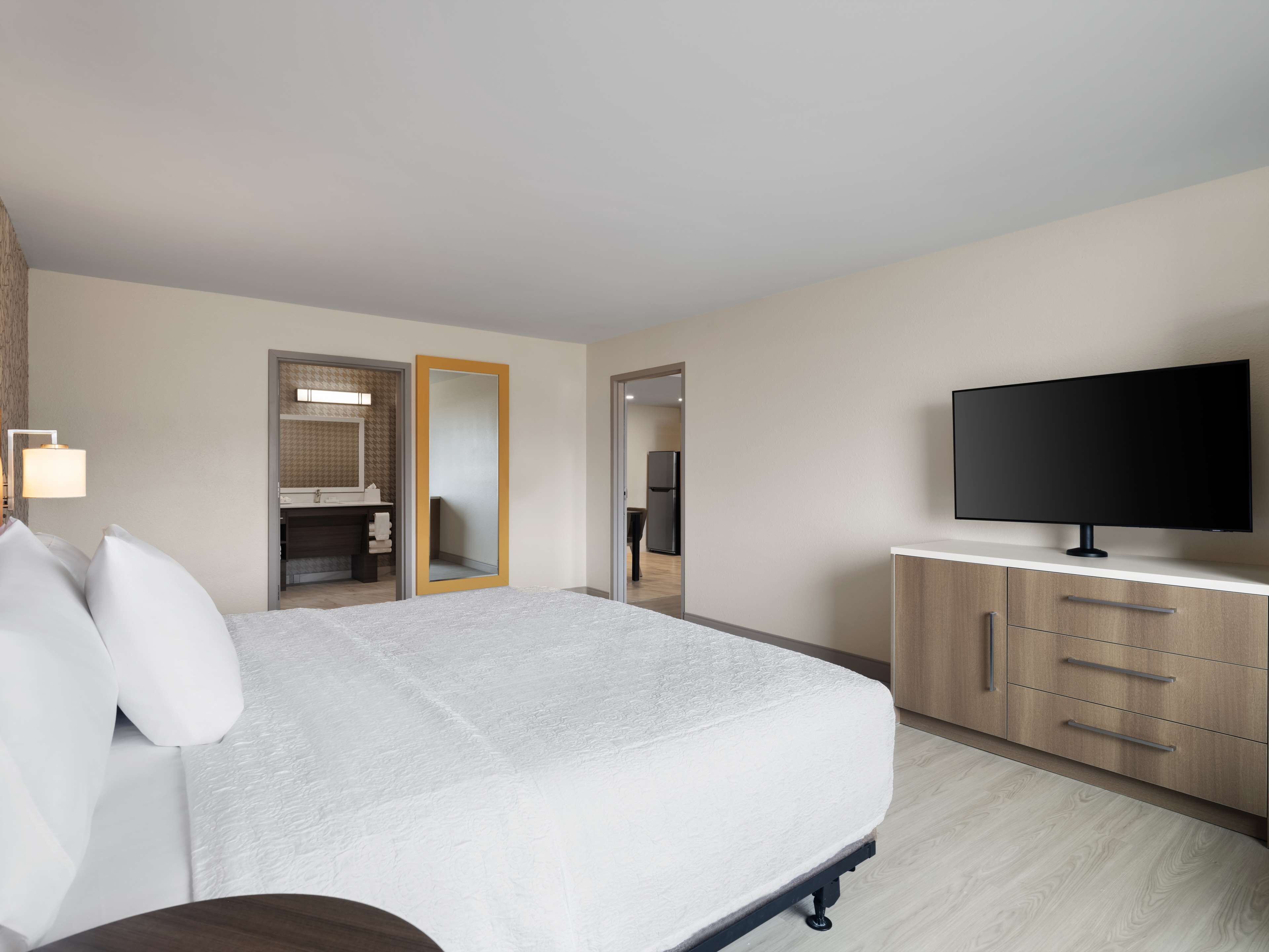 Habitación de hotel con cama, televisor, armario y baño visible a través de una puerta abierta.
