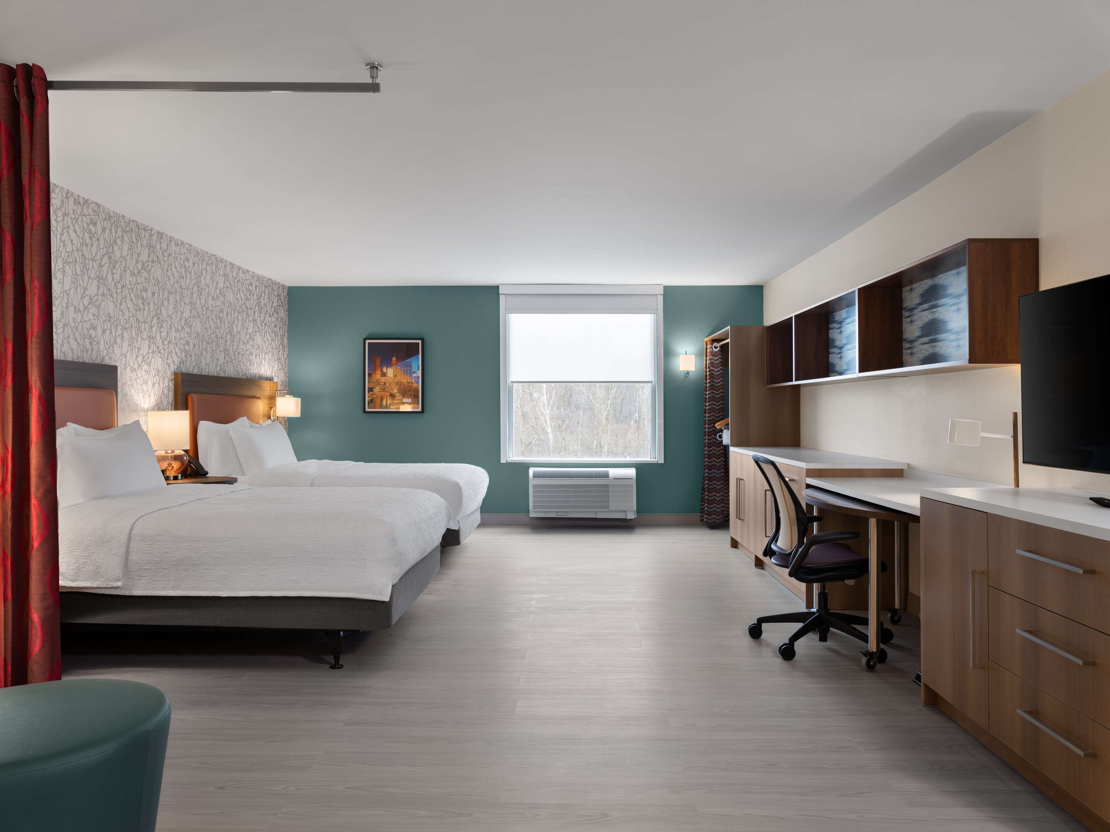 A hotel room with two beds, a desk, a chair, a TV, and a window with a view.