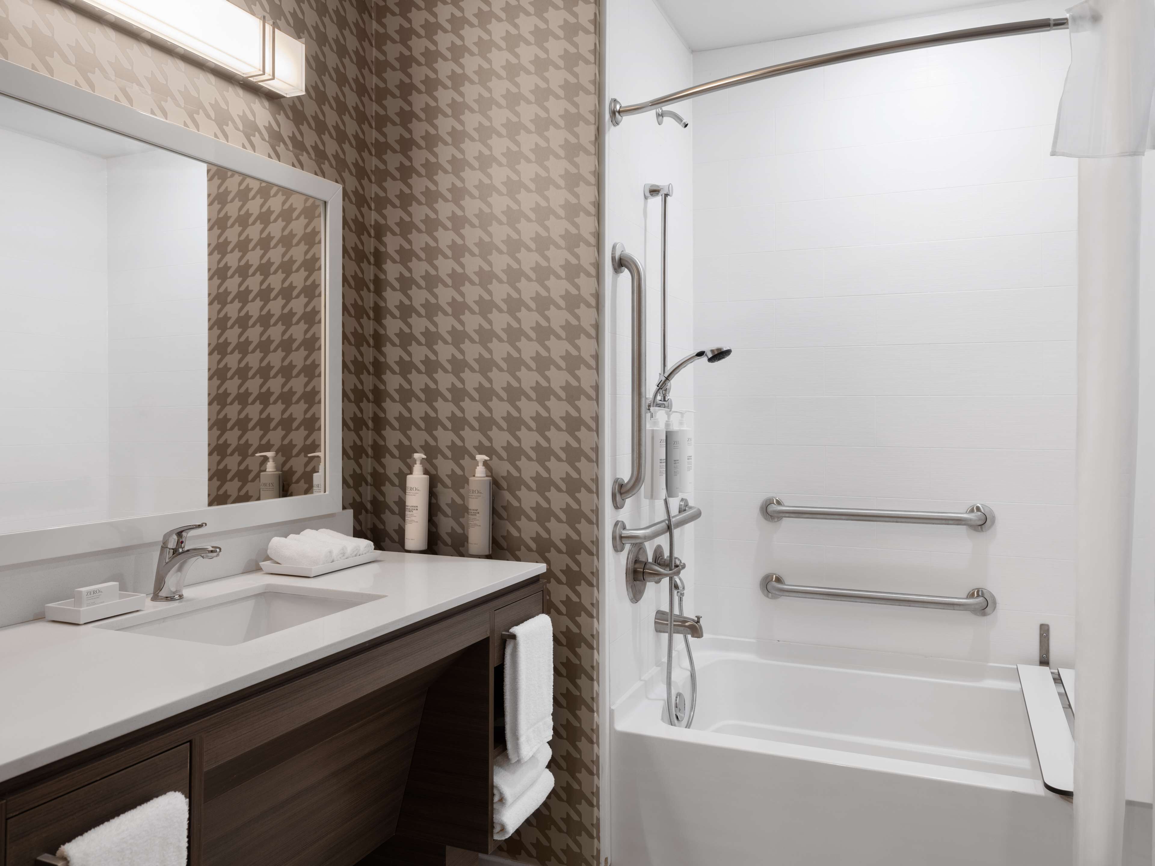 Un baño moderno con tocador doble, un espejo grande y una ducha a pie con barras de apoyo.