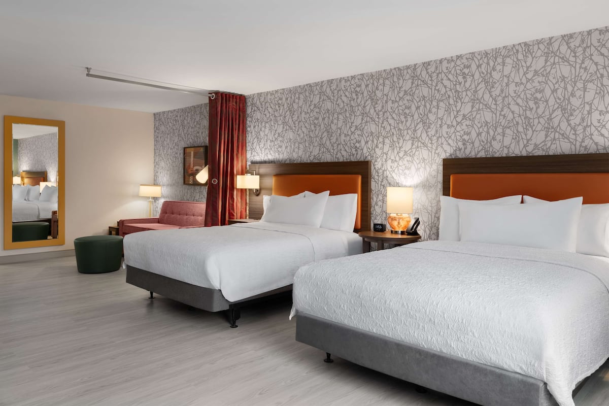 Ein Hotelzimmer mit zwei Betten, einem großen Spiegel, einem roten Vorhang und einer Wand mit Muster.