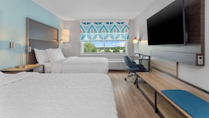 A hotel room with two beds, a desk, a TV, and a window with a view.