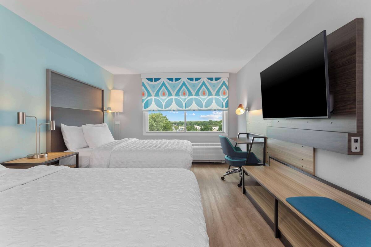 Habitació d'hotel amb dos llits, un escriptori, una televisió i una finestra amb vistes.