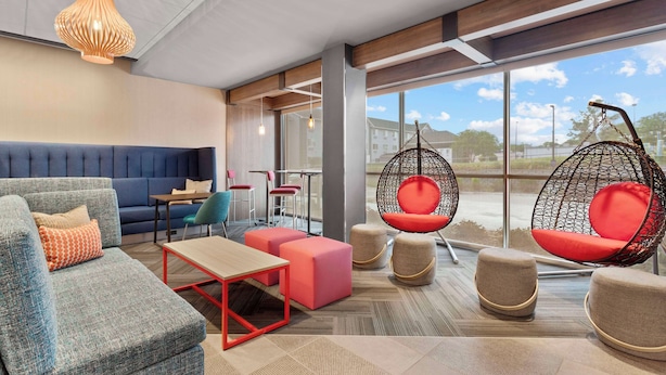 A modern lounge area with seating options including sofas, ottomans, and hanging chairs, a wooden coffee table, and large windows offering a view of the outdoors.