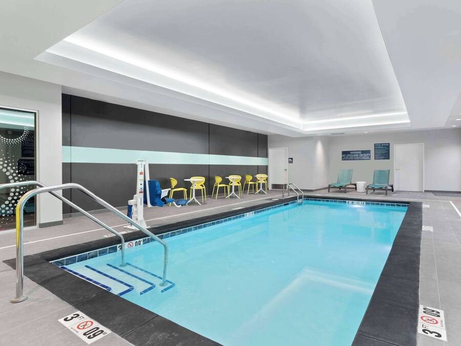 A modern indoor swimming pool with clear lane markings, safety signs, and lounge chairs.